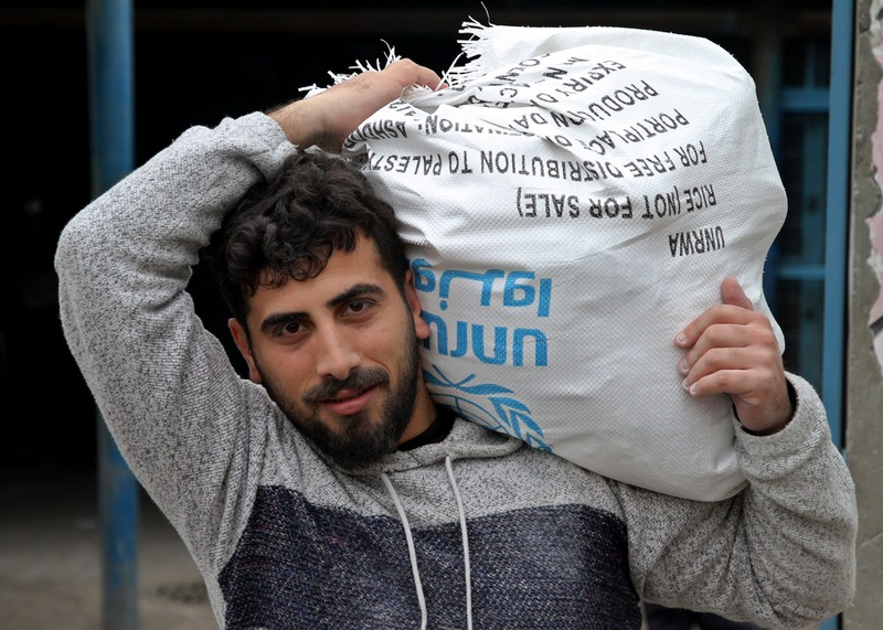 Un travailleur palestinien porte un sac de farine dans un centre de distribution de l'Office de secours et de travaux des Nations Unies pour les réfugiés de Palestine dans le Proche-Orient (UNRWA) dans le camp de réfugiés d'Al-Shati à Gaza, le 23 février 2021. (Xinhua/Rizek Abdeljawad)
