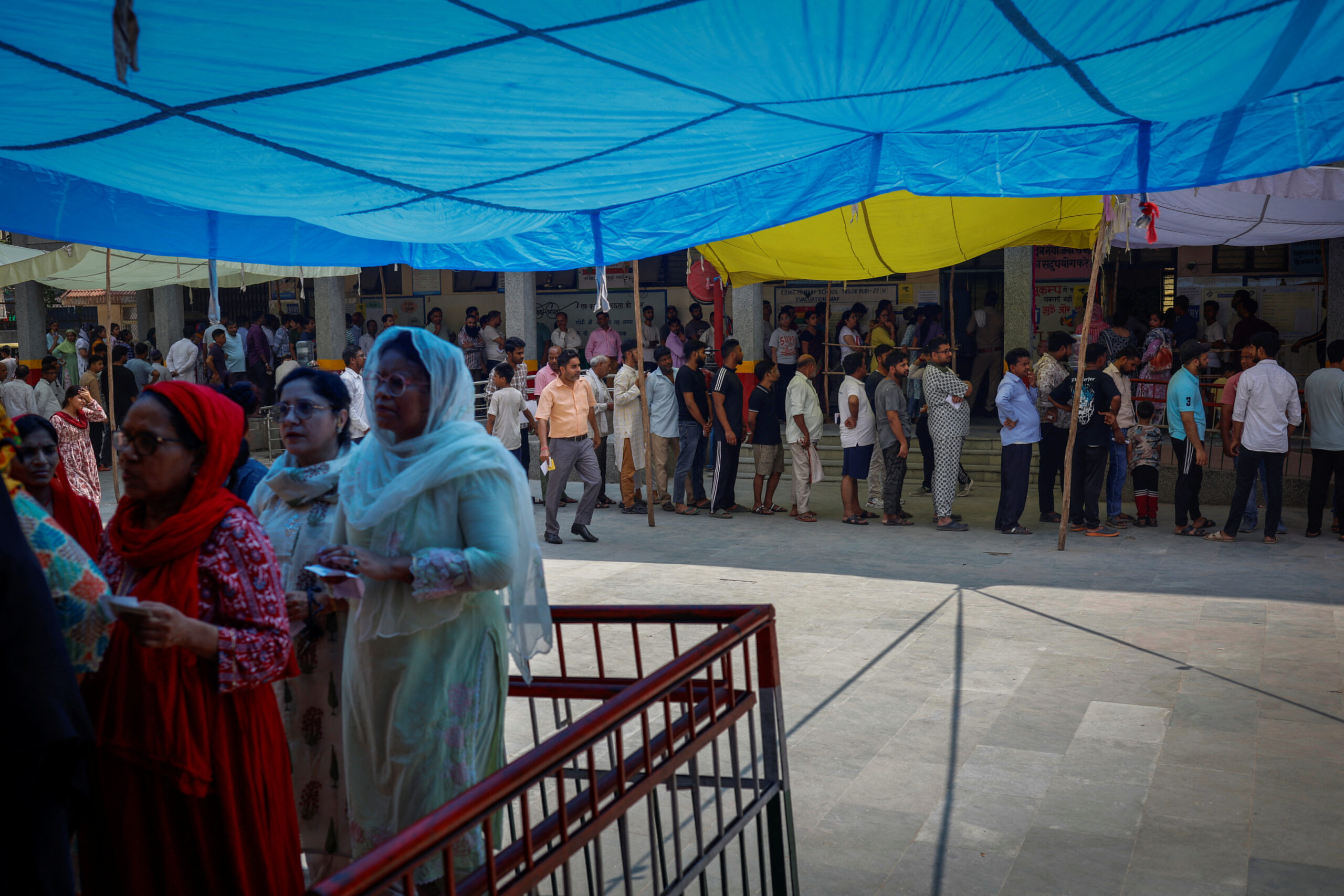 Des électeurs se tiennent à l'ombre par une chaude journée d'été, alors qu'ils attendent de voter dans un bureau de vote lors de la sixième phase des élections générales, à New Delhi, en Inde. /Photo prise le 25 mai 2024/REUTERS/Adnan Abidi