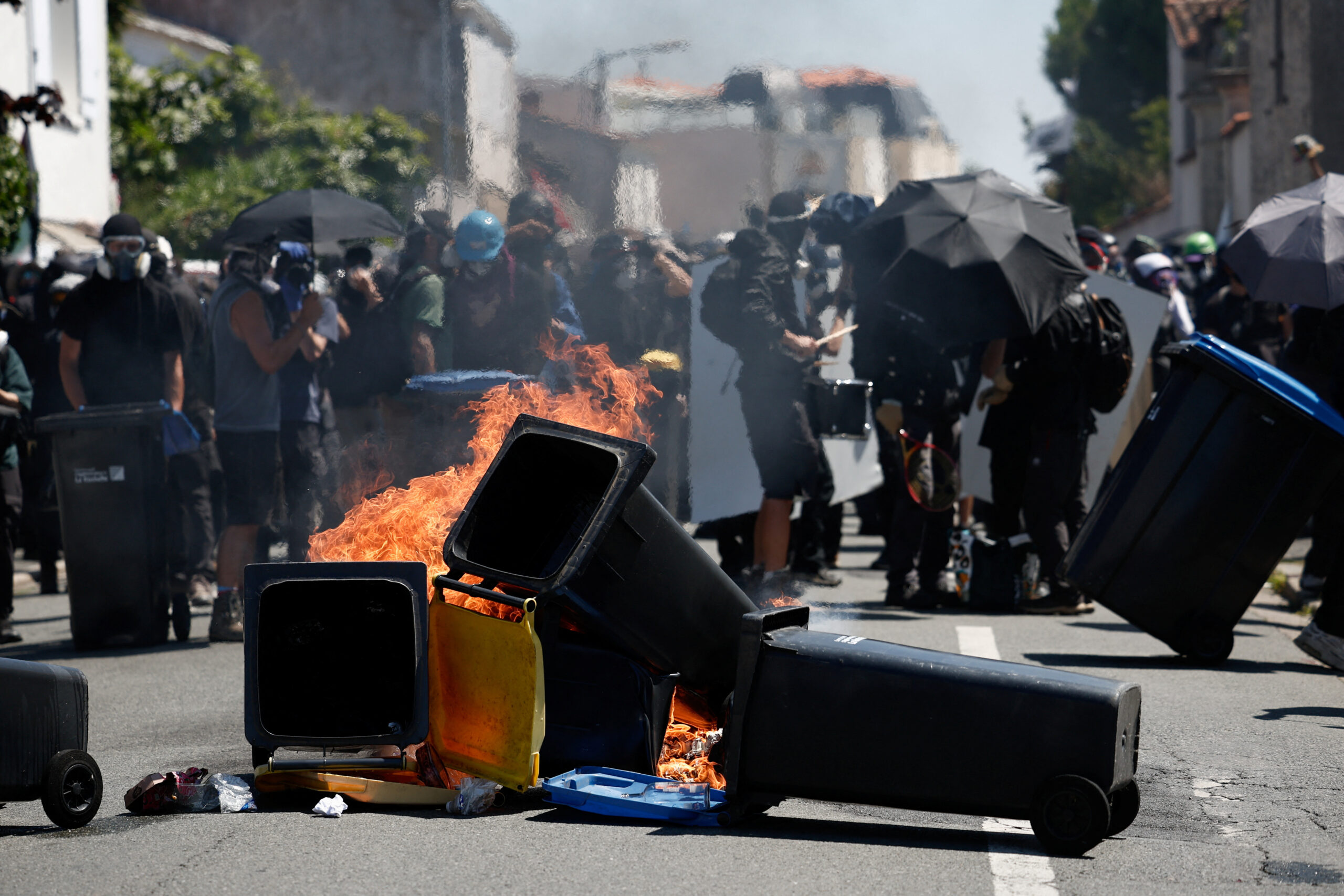 Des manifestants se tiennent derrière des poubelles en feu lors d'une manifestation pour bloquer le terminal agro-industriel du Port de la Pallice, dans le cadre des journées de protestation « Stop Méga-Bassines » contre les méga-bassins d'eau de l'agro-industrie, à La Rochelle/Photo prise France, 20 juillet 2024/ REUTERS/Benoit Tessier