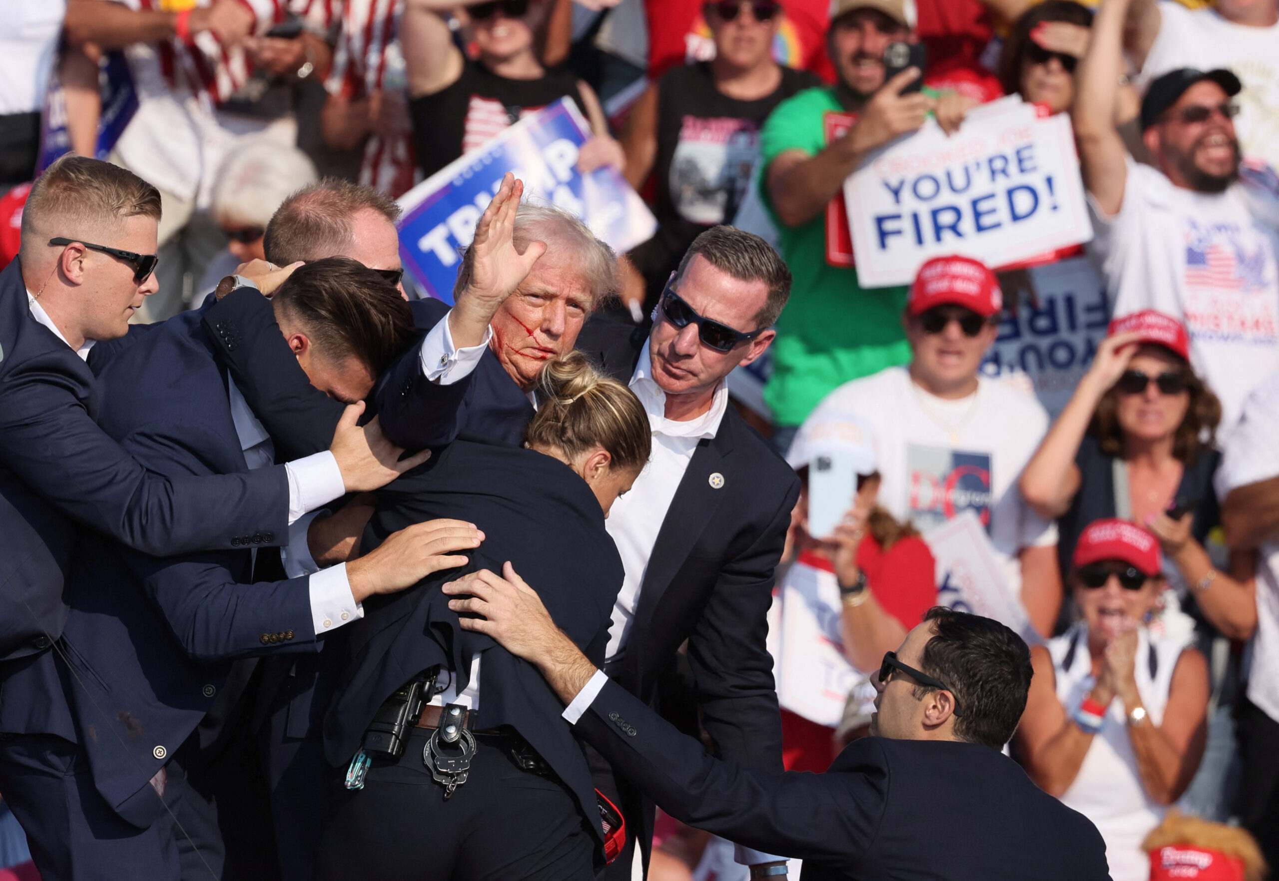 Le candidat républicain à la présidence et ancien président des États-Unis Donald Trump fait des gestes avec un visage ensanglanté alors qu'il est assisté par le personnel des services secrets américains après avoir reçu une balle dans l'oreille droite lors d'un rassemblement de campagne au Butler Farm Show à Butler, Pennsylvanie, États-Unis, le 13 juillet 2024. REUTERS/Brendan McDermid