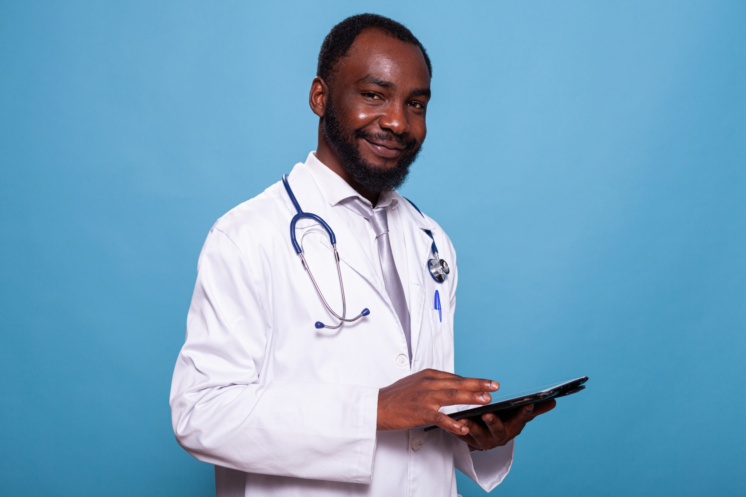 Portrait d'un médecin avec stéthoscope souriant à la caméra tenant une tablette à écran tactile portant l'uniforme de l'hôpital. Médecin heureux en blouse de laboratoire à l'aide d'un appareil numérique.