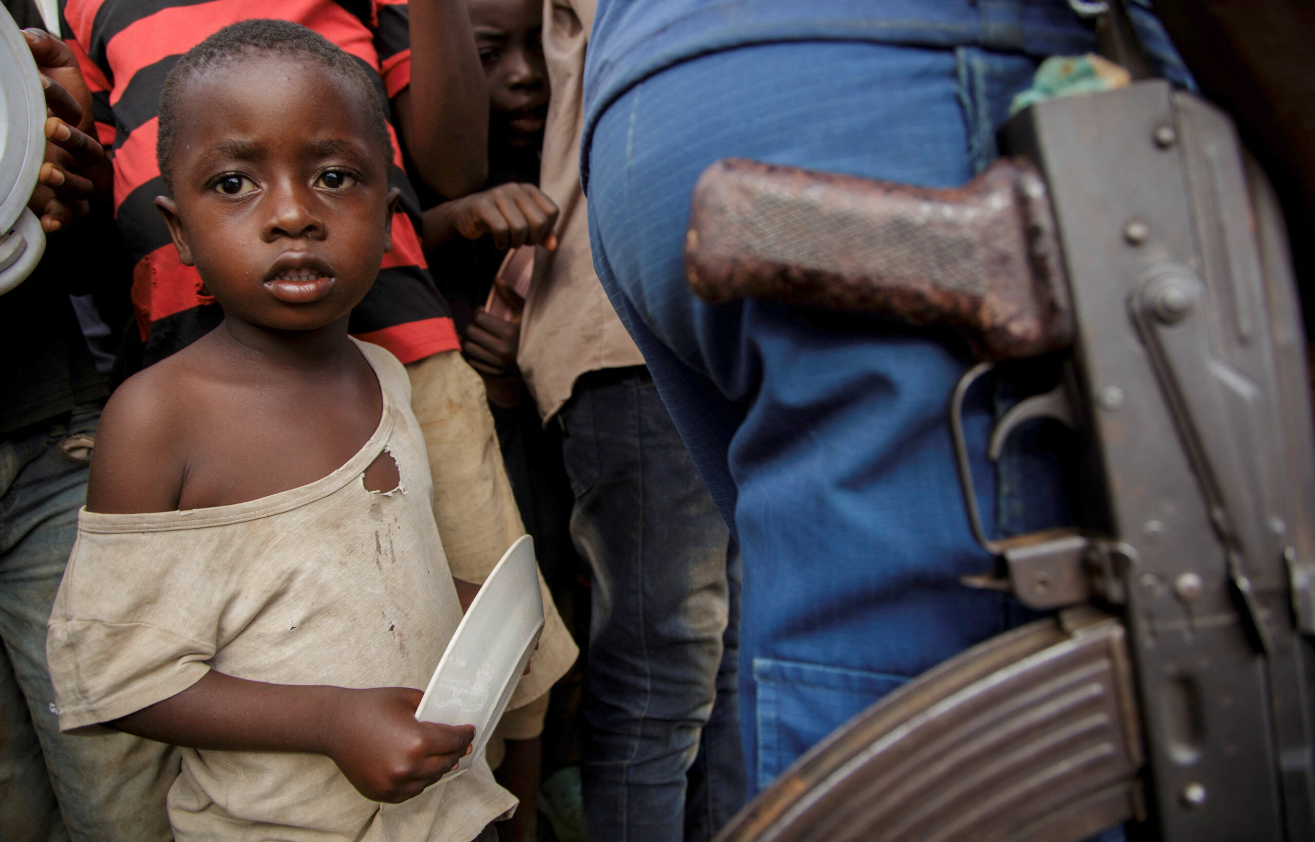 Un enfant congolais se tient à côté d'un policier tandis que des personnes attendent de recevoir de l'aide alimentaire de bénévoles burundais au stade de Rugombo, après avoir fui les nouveaux affrontements entre les rebelles du M23 et les Forces armées de la République démocratique du Congo (FARDC), dans la commune de Rugombo de la province de Cibitoke, au Burundi. /Photo prise le 18 février 2025/REUTERS/Evrard Ngendakumana