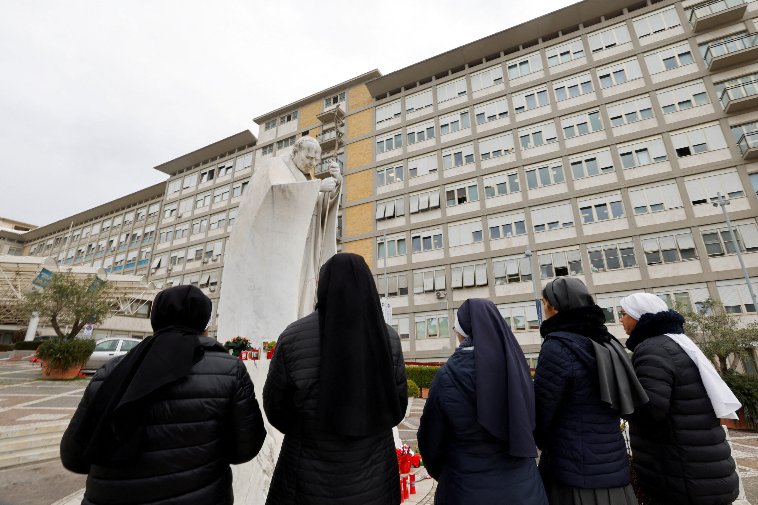 Des religieuses prient devant la statue du défunt pape Jean-Paul II à l'extérieur de l'hôpital Gemelli où le pape François est admis pour traitement, à Rome. /Photo prise le 24 février 2025/REUTERS/Ciro De Luca