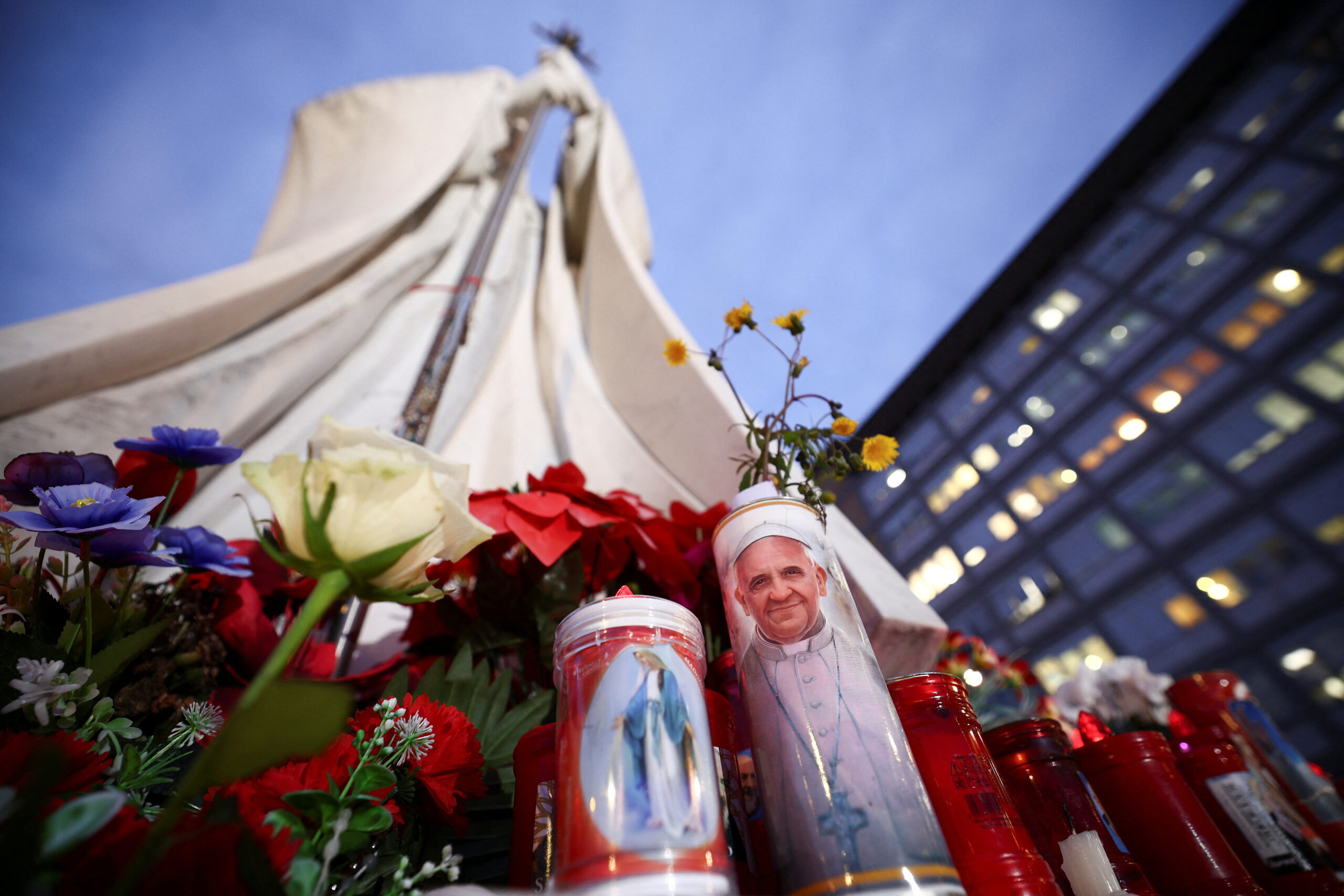 Une bougie portant une image du pape François est posée à côté de la statue du défunt pape Jean-Paul II, à Rome, en Italie. /Photo prise le 20 février 2025/REUTERS/Guglielmo Mangiapane